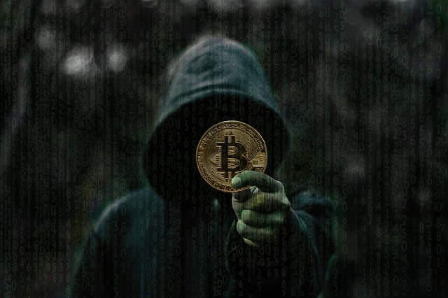 grafika człowieka z kapturem i moneta bitcoina w dłoni